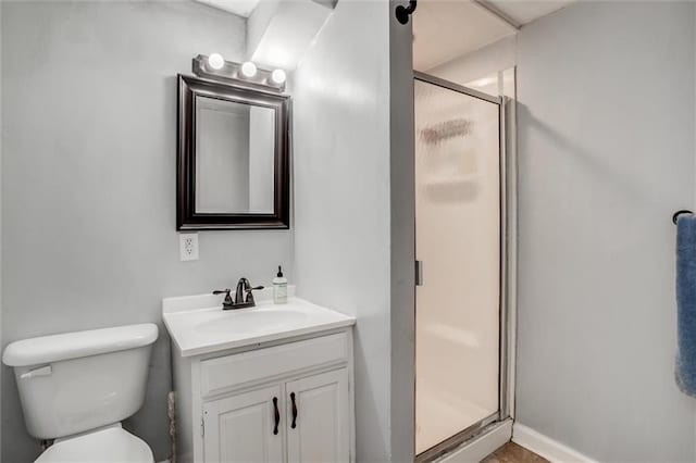 bathroom with toilet, a shower stall, baseboards, and vanity