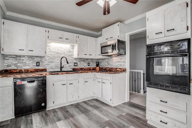 kitchen with a sink, white cabinetry, ornamental molding, black appliances, and dark countertops