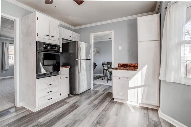 kitchen with crown molding, freestanding refrigerator, white cabinets, ceiling fan, and oven