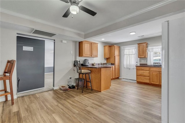 kitchen featuring ceiling fan, light hardwood / wood-style floors, kitchen peninsula, a breakfast bar, and crown molding