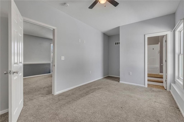 unfurnished bedroom featuring ceiling fan, light colored carpet, multiple windows, and ensuite bath