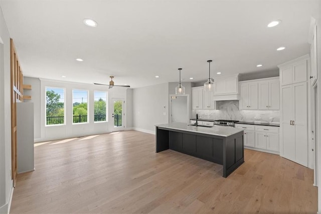 kitchen featuring decorative light fixtures, white cabinetry, a kitchen island with sink, and tasteful backsplash