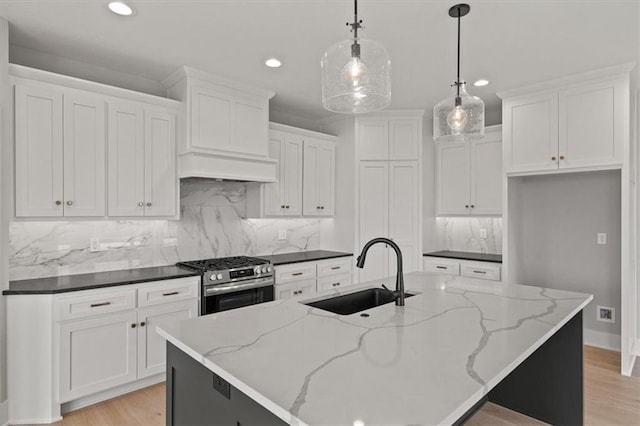 kitchen featuring high end stainless steel range oven, sink, pendant lighting, white cabinetry, and an island with sink