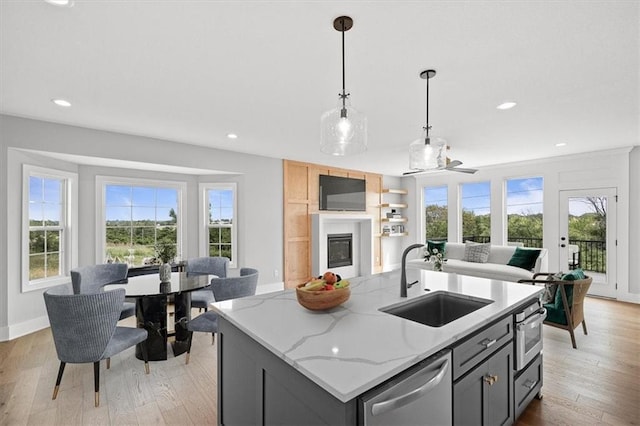 kitchen featuring sink, stainless steel appliances, light stone counters, gray cabinets, and a center island with sink