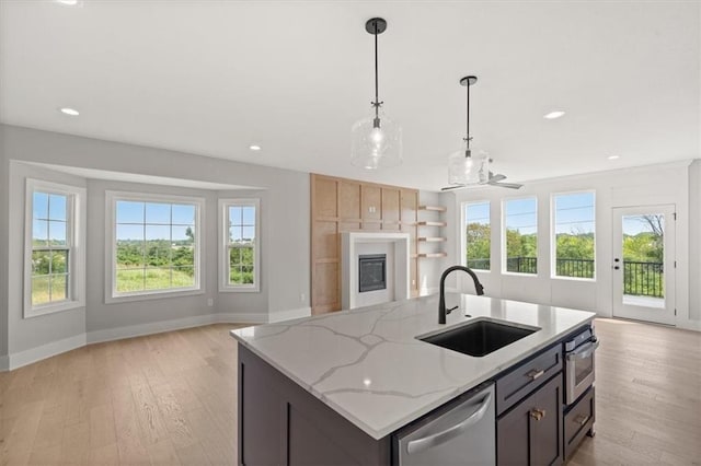 kitchen with sink, light stone counters, decorative light fixtures, a center island with sink, and appliances with stainless steel finishes