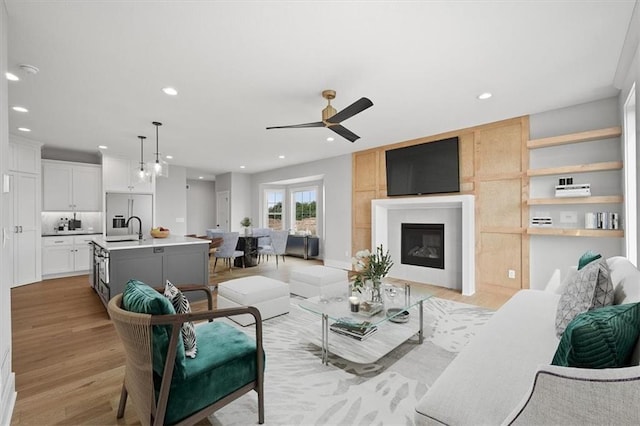 living room with a fireplace, ceiling fan, sink, and light hardwood / wood-style floors