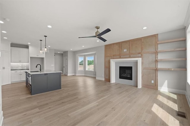 kitchen featuring ceiling fan, a kitchen island with sink, sink, pendant lighting, and white cabinets