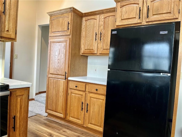 kitchen featuring black fridge, hardwood / wood-style floors, decorative backsplash, and stove