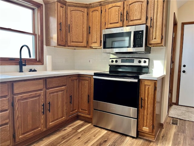 kitchen featuring sink, decorative backsplash, light hardwood / wood-style flooring, and stainless steel appliances