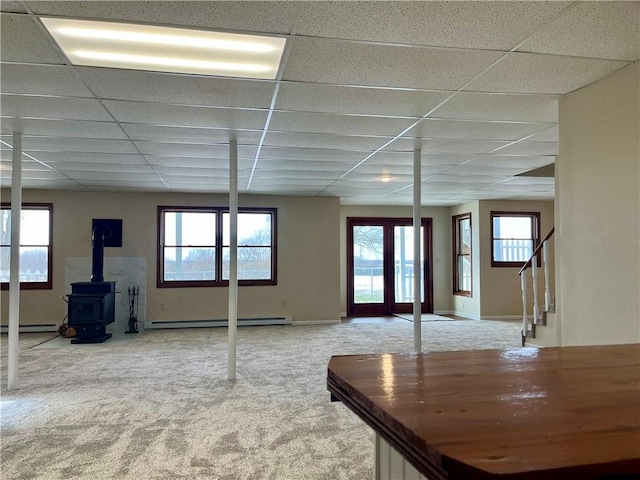 interior space featuring a drop ceiling, a baseboard radiator, a wood stove, and carpet flooring