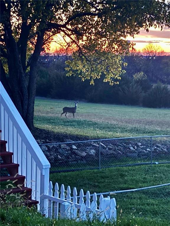 yard at dusk featuring a rural view and fence