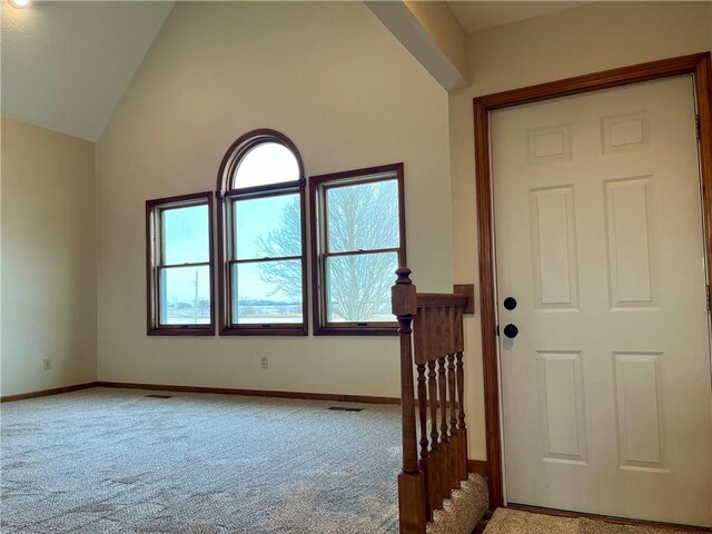 carpeted entrance foyer featuring visible vents, high vaulted ceiling, and baseboards