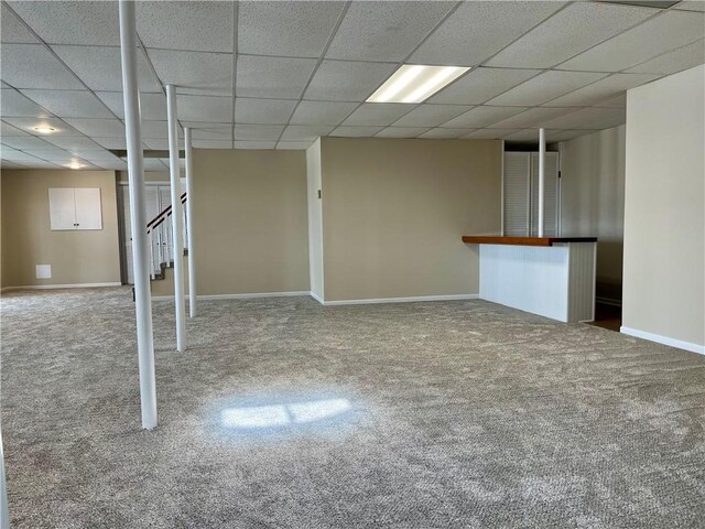 finished below grade area with stairway, a paneled ceiling, baseboards, and carpet floors