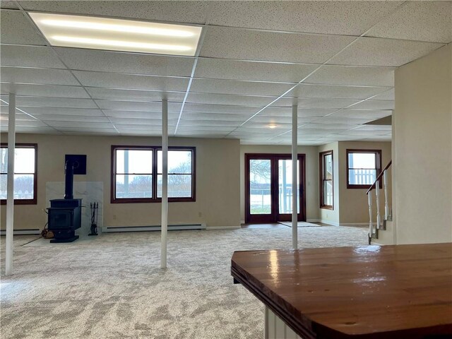 interior space featuring a drop ceiling, stairs, carpet, a baseboard radiator, and a wood stove