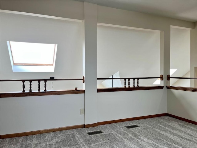 carpeted empty room with visible vents, baseboards, and a skylight