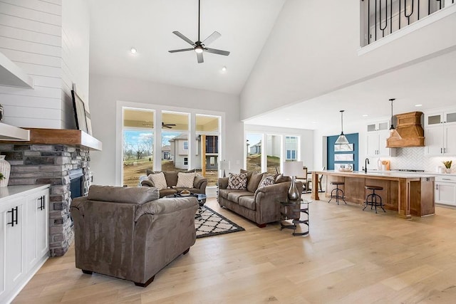 living room with a stone fireplace, sink, high vaulted ceiling, and light hardwood / wood-style flooring