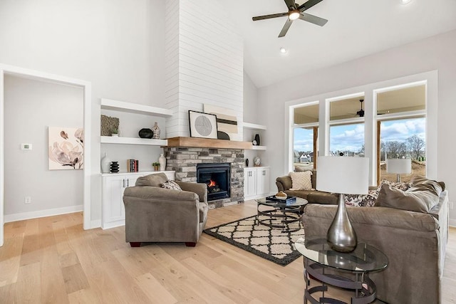 living room with built in shelves, light wood-type flooring, high vaulted ceiling, and a stone fireplace