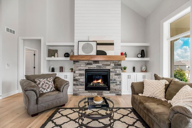 living room featuring built in shelves, light hardwood / wood-style floors, a stone fireplace, and high vaulted ceiling