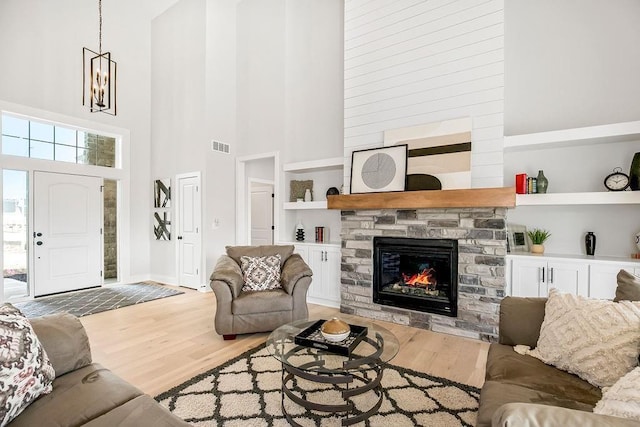 living room featuring a high ceiling, a stone fireplace, hardwood / wood-style flooring, built in shelves, and a chandelier