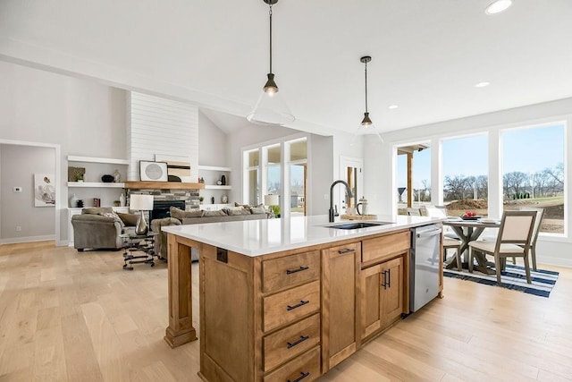 kitchen with stainless steel dishwasher, a kitchen island with sink, sink, pendant lighting, and a fireplace