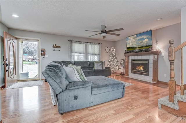 living room with ceiling fan, a fireplace, a textured ceiling, and light hardwood / wood-style flooring