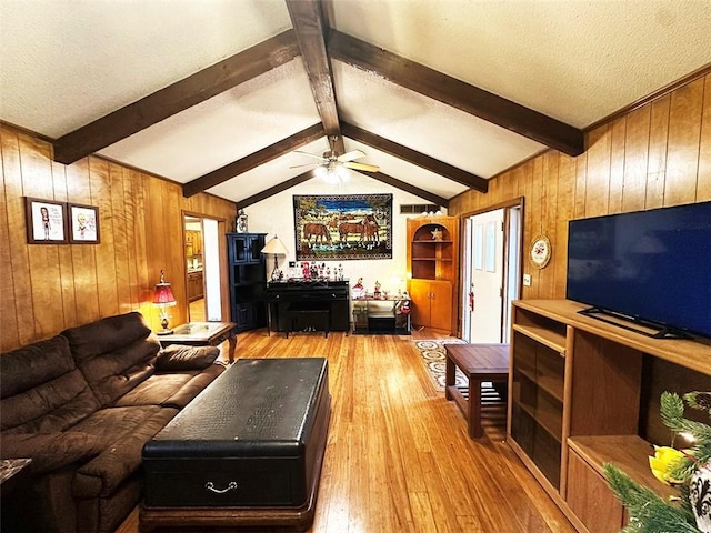 living room featuring light wood-type flooring, vaulted ceiling with beams, ceiling fan, and wooden walls