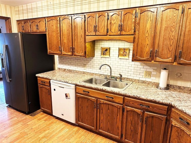 kitchen with light stone countertops, sink, stainless steel fridge, white dishwasher, and light wood-type flooring