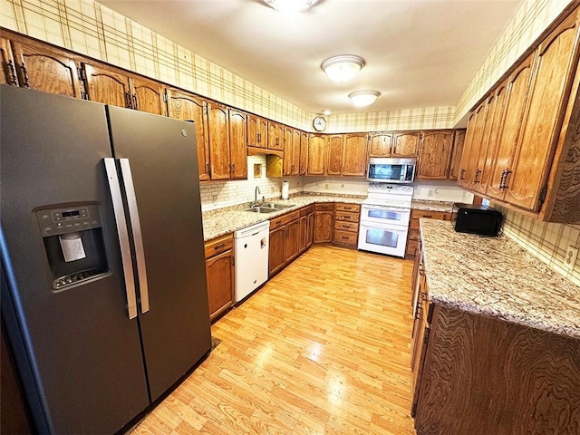 kitchen featuring light stone countertops, tasteful backsplash, stainless steel appliances, sink, and light hardwood / wood-style flooring