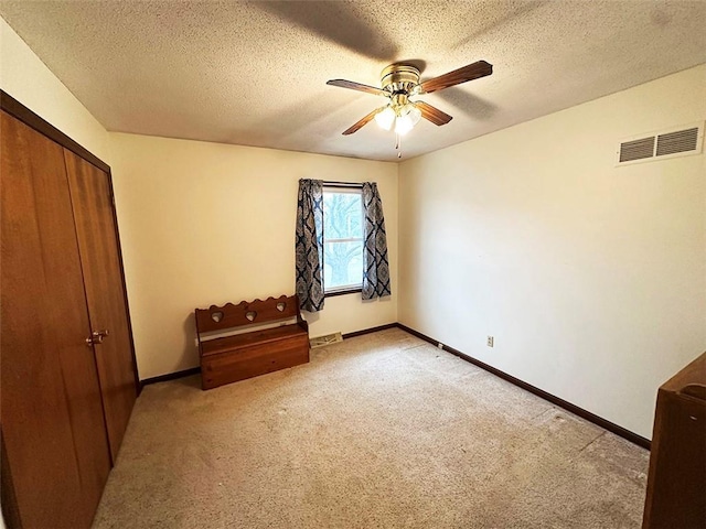 unfurnished bedroom featuring ceiling fan, a closet, light colored carpet, and a textured ceiling