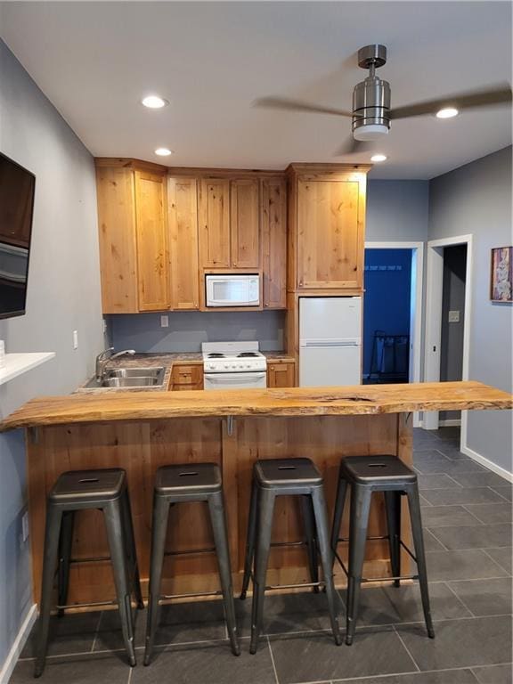 kitchen featuring sink, kitchen peninsula, decorative light fixtures, white appliances, and a breakfast bar area