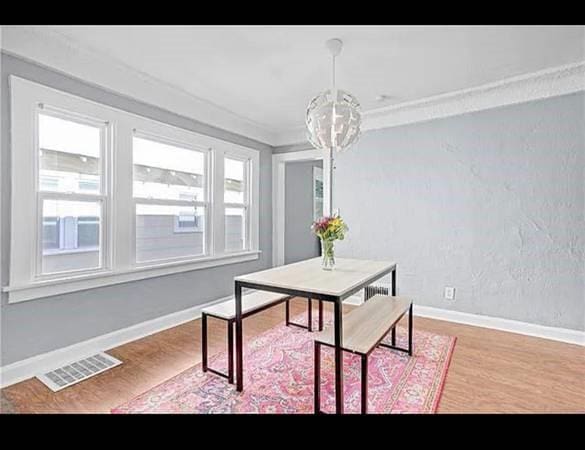 dining space featuring crown molding, wood-type flooring, and a notable chandelier