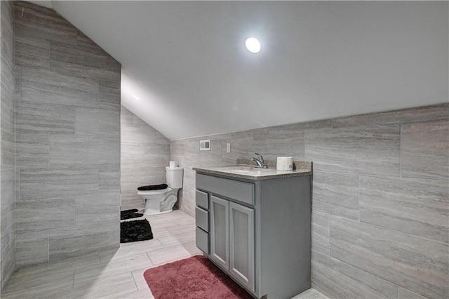 bathroom with tile patterned floors, lofted ceiling, toilet, vanity, and tile walls