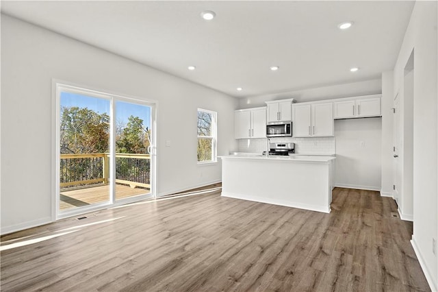 kitchen with white cabinets, a center island with sink, tasteful backsplash, light hardwood / wood-style floors, and stainless steel appliances