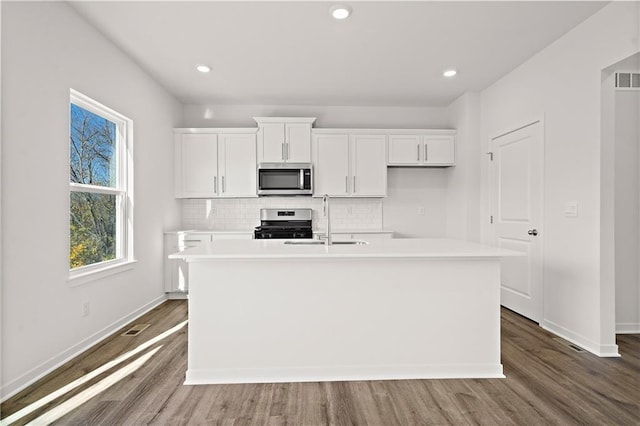 kitchen featuring white cabinets, sink, stainless steel appliances, and an island with sink