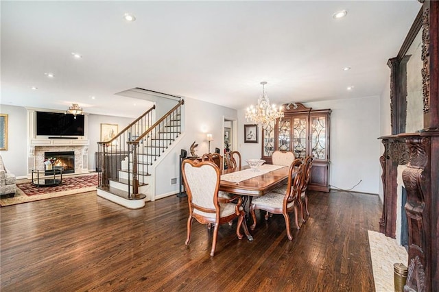 dining area featuring a glass covered fireplace, wood finished floors, stairway, a chandelier, and recessed lighting