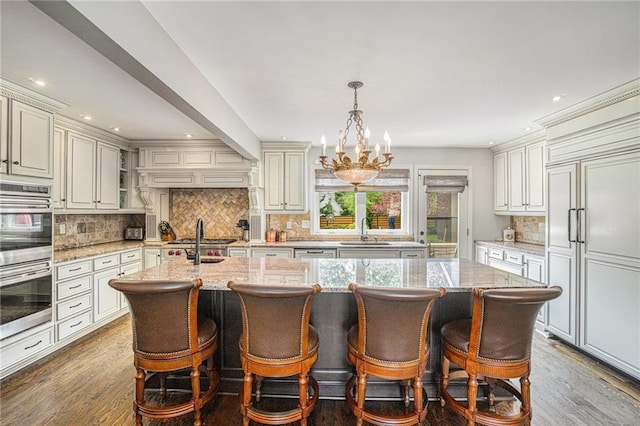 821 W 54th Ter, Kansas City, MO 64112 - kitchen with appliances with stainless steel finishes, backsplash, a center island with sink, dark wood finished floors, and recessed lighting
