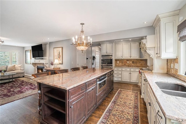 821 W 54th Ter, Kansas City, MO 64112 - kitchen featuring a lit fireplace, a chandelier, dark wood-style flooring, a spacious island, and recessed lighting