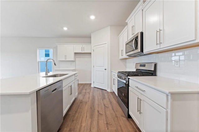 kitchen featuring white cabinetry, sink, stainless steel appliances, wood-type flooring, and a center island with sink