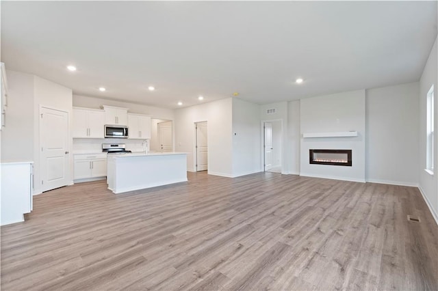 kitchen with a center island with sink, white cabinetry, light wood-type flooring, and range