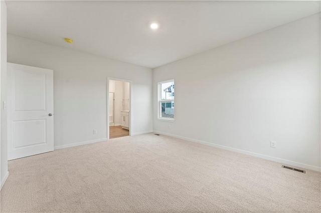 unfurnished bedroom featuring light carpet and ensuite bathroom