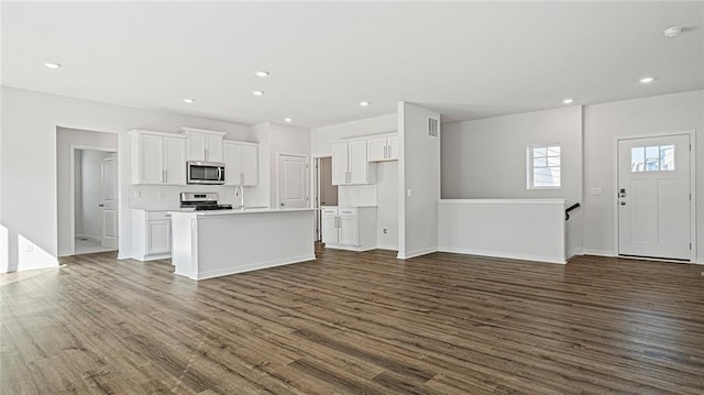 kitchen featuring stove, dark hardwood / wood-style flooring, backsplash, a center island with sink, and white cabinetry