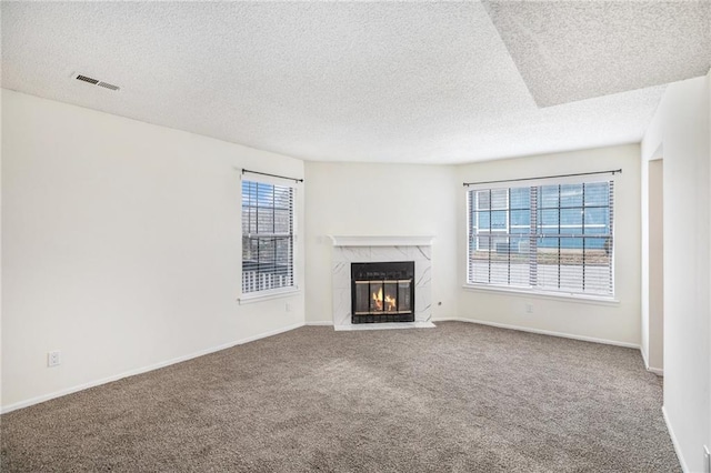 unfurnished living room with carpet flooring, a textured ceiling, a healthy amount of sunlight, and a premium fireplace