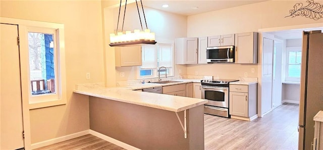 kitchen with sink, light hardwood / wood-style flooring, kitchen peninsula, decorative light fixtures, and appliances with stainless steel finishes