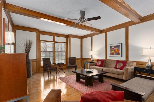 living room featuring beam ceiling, ceiling fan, light hardwood / wood-style flooring, and a textured ceiling