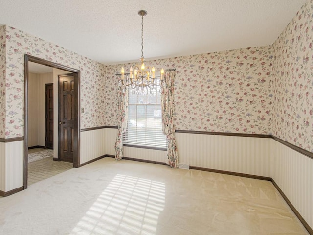 unfurnished dining area with a notable chandelier, light colored carpet, and a textured ceiling