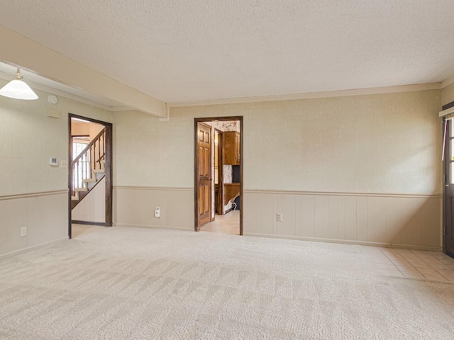 carpeted empty room featuring beamed ceiling and a textured ceiling