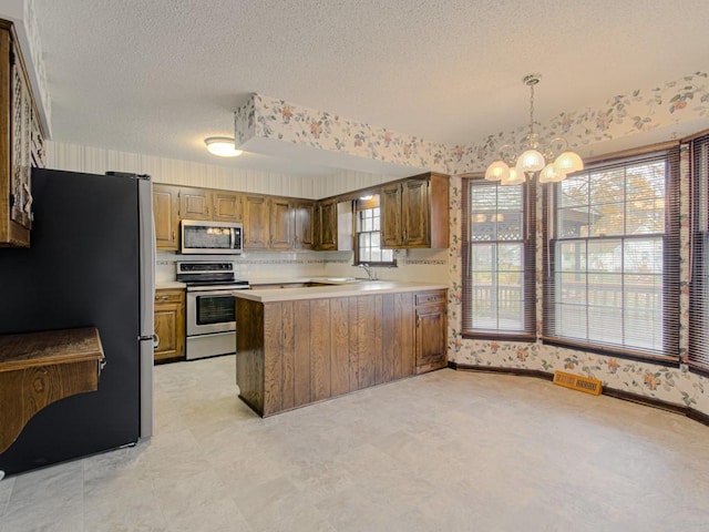 kitchen with kitchen peninsula, appliances with stainless steel finishes, a wealth of natural light, decorative light fixtures, and a notable chandelier