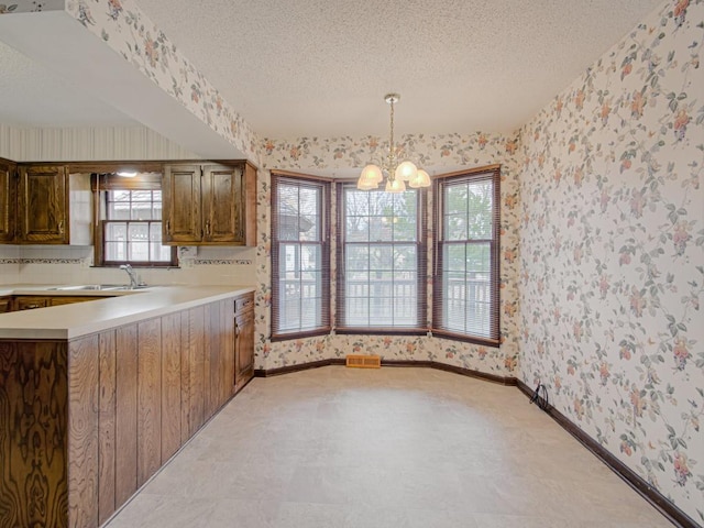 kitchen featuring sink, pendant lighting, a textured ceiling, and an inviting chandelier