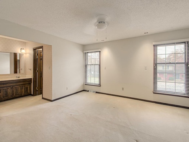 unfurnished bedroom featuring multiple windows, ceiling fan, light colored carpet, and ensuite bathroom