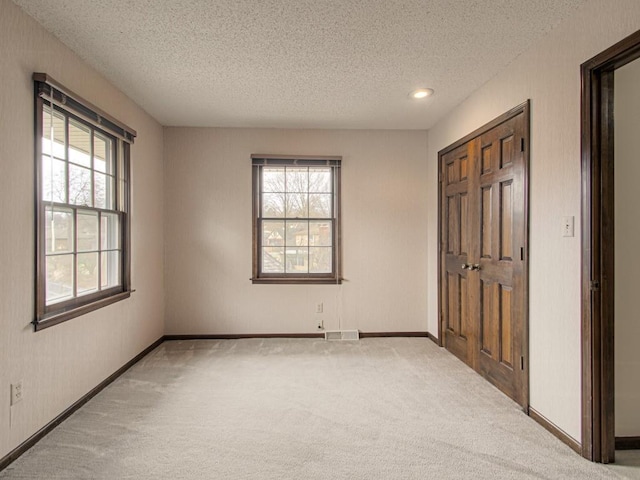 unfurnished bedroom featuring a closet, light colored carpet, a textured ceiling, and multiple windows